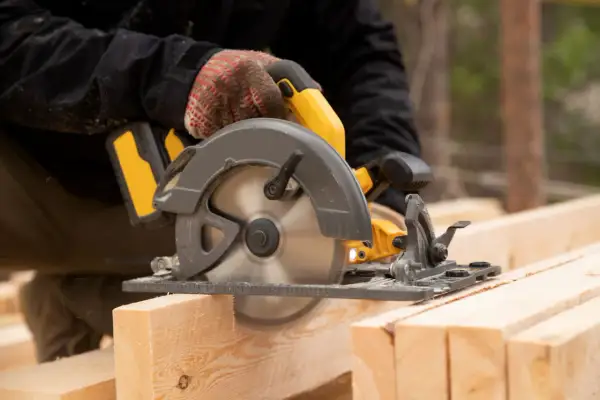 Main d'un bricoleur utilisant une scie circulaire pour couper du bois. La scie a une hauteur de coupe de 200 mm.