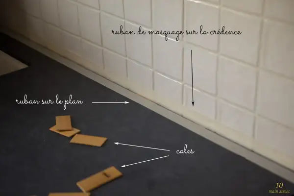 Préparation pour la pose d'un nouveau plan de travail : ruban de masquage sur la crédence et cales en bois sur le plan actuel.