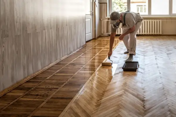 Un homme applique du vitrificateur sur un parquet. Le temps de séchage vitrificateur est crucial pour un résultat parfait.