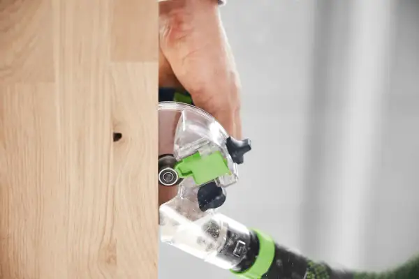 Main d'un artisan utilisant la défonceuse Festool OFK 500 pour travailler le bois avec précision.