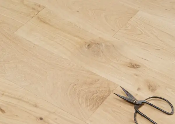 Un parquet en chêne clair, avec des ciseaux posés dessus. Peut-on laisser un parquet brut ? La réponse est oui, pour un style naturel.