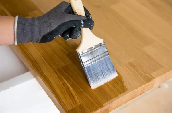 Application d'huile de lin au pinceau sur un plateau en bois. La finition protège et sublime le grain du bois.