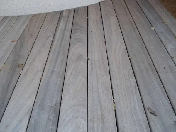 Planches de bois grisé, patinées par le temps, formant une terrasse. Quelques feuilles mortes parsèment le sol.