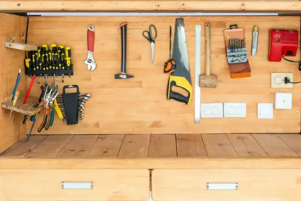 Un établi en bois bien rangé avec des outils : tournevis, clés, scie, marteau, ciseaux, et une boîte de forets.