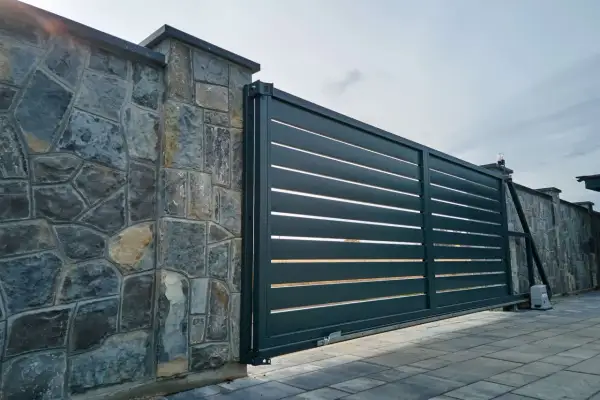 Portail coulissant moderne en aluminium anthracite, juxtaposé à un mur en pierres naturelles. Le portail est en pose, prêt à sécuriser l'entrée.