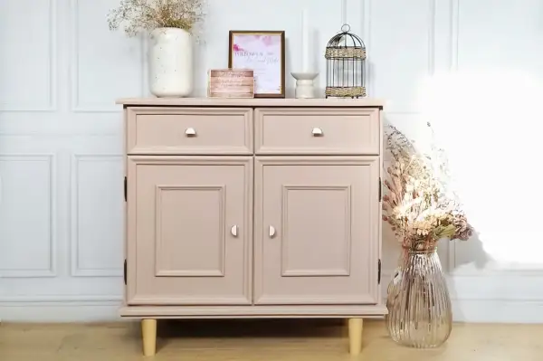 Un meuble en bois, fraîchement peint en rose poudré, est décoré de fleurs séchées et d'une cage à oiseaux.