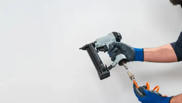 Main d'un bricoleur connectant un tuyau à un pistolet à clous pneumatique, un outil essentiel pour tout projet de menuiserie.