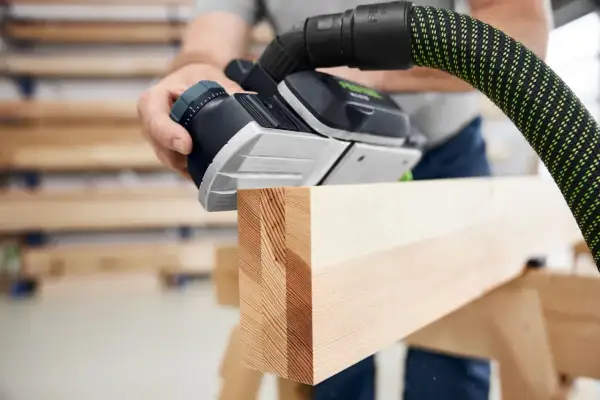 Main d'un artisan utilisant une raboteuse Festool pour lisser une pièce de bois.