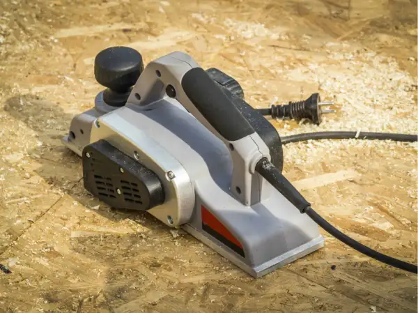 Une raboteuse électrique, prête à aplanir le bois, repose sur un chantier jonché de copeaux.