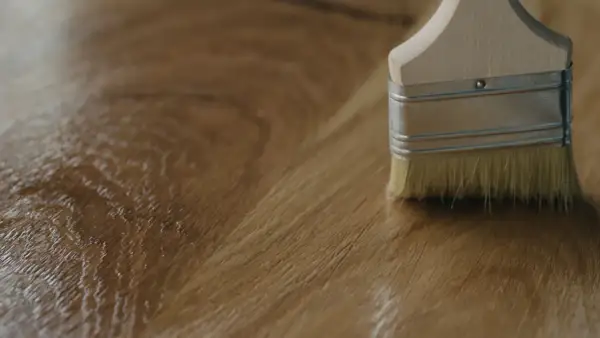 Application d'un vernis ou huile pour bois avec un pinceau sur une surface en bois.
