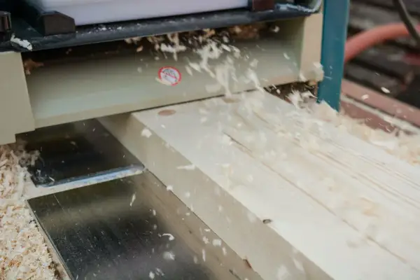 Le bois est raboté avec précision par la dégau rabot, créant une surface lisse et des copeaux fins qui volent dans l'air.