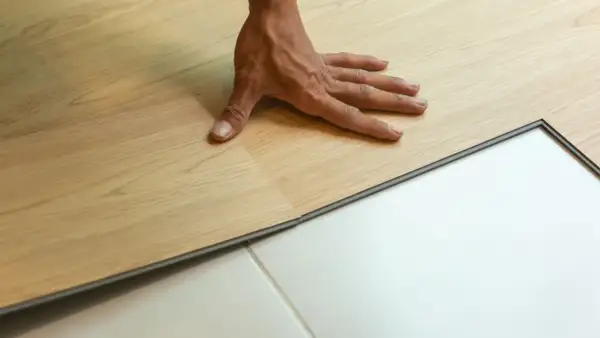 Pose d'un parquet stratifié imitation bois clair. Une main ajuste une lame sur un sol blanc.