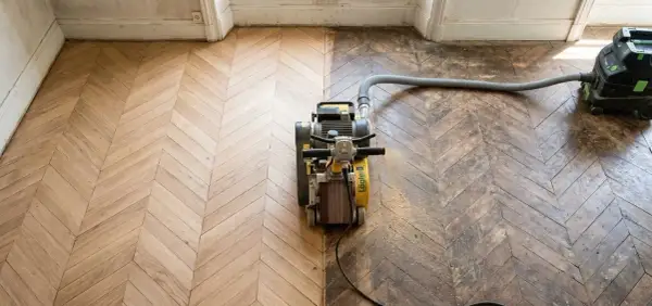 Ponçage d'un parquet ancien en chevrons, révélant sa beauté. Le prix du ponçage parquet dépend de l'état. Aspirateur industriel en action.