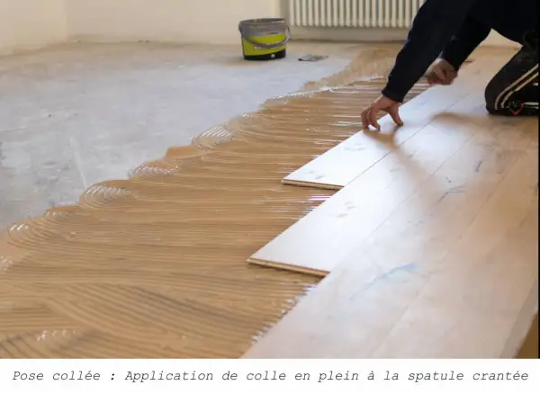 Pose de parquet collé : application de colle en plein à la spatule crantée, avant la pose des lames de bois.