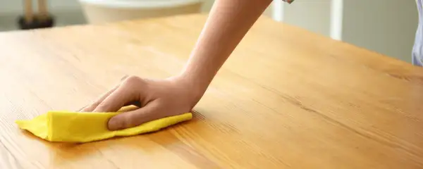 Main d'enfant nettoyant une table en bois avec un chiffon jaune. Apprenez comment nettoyer une table en bois pour un éclat parfait.