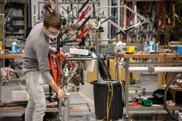 Un ouvrier assemble un vélo rouge, peut-être une création de la marque Korman, dans un atelier rempli de cadres.