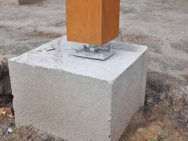 Un poteau en bois est fixé sur un plot béton à enterrer, prêt pour une construction solide.