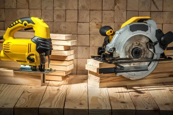Scie sauteuse jaune et scie circulaire argentée, prêtes à découper du bois. La différence entre ces outils est claire pour tout bricoleur.