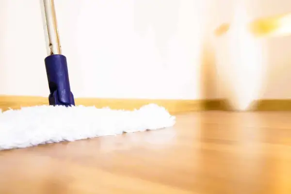 Une serpillère blanche et moelleuse nettoie un parquet brillant. La lumière douce éclaire la scène, créant une ambiance chaleureuse.