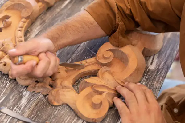 Un artisan utilise un ciseau pour sculpter le bois, créant des volutes complexes sur une pièce ornementale.
