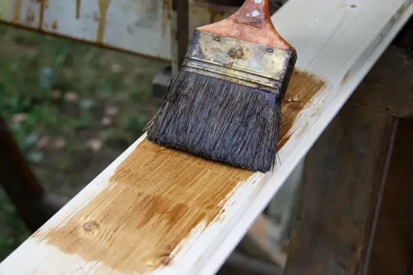 Application d'une lasure effet bois blanchi sur une planche de bois clair. Le pinceau dépose une fine couche de produit.