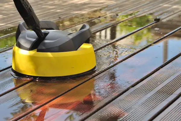 Nettoyer terrasse bois savon noir : un nettoyeur haute pression jaune et noir en action sur des lattes de bois mouillées.