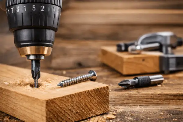 Apprenez comment utiliser une perceuse pour visser dans le bois. Une mèche est dans le bois, une vis à côté.